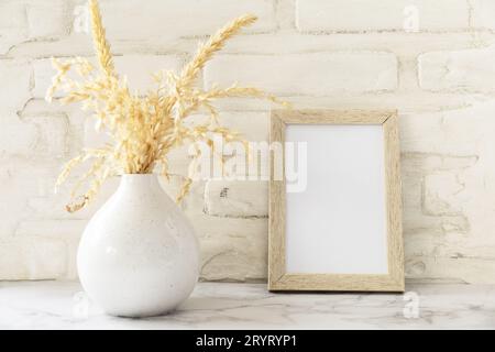 White picture frame mockup. White wall background. Scandinavian interior, neutral color palette with dry grass. Selective focus. Stock Photo