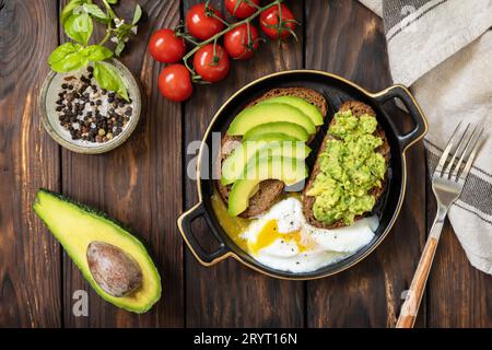 Healthy breakfast, sandwich with avocado and egg. Wholemeal bread toast sliced avocado and poached egg on a rustic table. View f Stock Photo