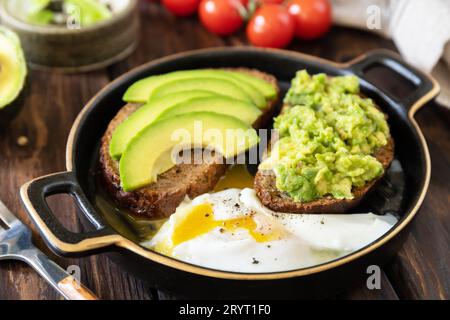Healthy breakfast, sandwich with avocado and egg. Wholemeal bread toast sliced avocado and poached egg on a rustic table. Stock Photo