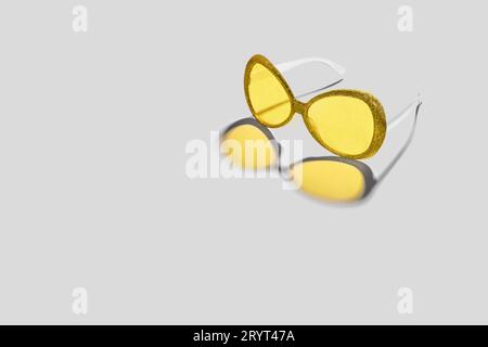 Trending colors of 2021. Plastic sunglasses with silver sparkles frame and yellow glasses. Yellow color shadow from glasses Stock Photo