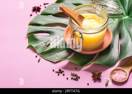 Ghee butter in a glass jar, pink salt and spices on pink background Stock Photo