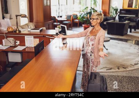 Mature woman comes to the hotel at the reception. She is tired of waiting for receptionist. Stock Photo