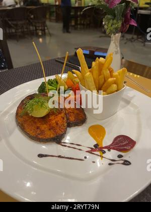 Fried kingfish on a white plate served with french fries and steamed vegetables. Stock Photo
