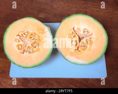 Freshly cut Rockmelon cut into half on a white cutting board in the kitchen. Stock Photo