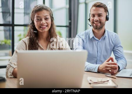 smilling man and charming woman are sitting at laptops in headphones Stock Photo