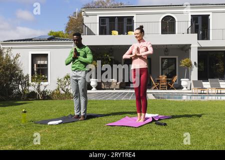 Diverse couple practicing yoga and meditating in garden Stock Photo