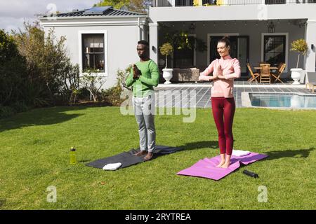 Diverse couple practicing yoga and meditating in garden Stock Photo