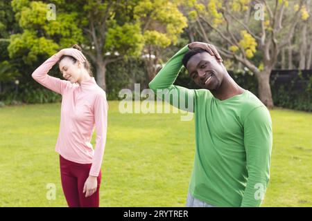 Happy diverse couple practicing yoga and stretching in garden Stock Photo