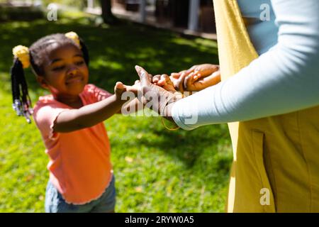 Midsection of african american mother holding daughter's hands in backyard on sunny day Stock Photo