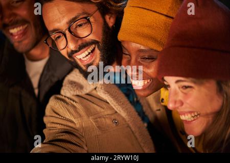 Young adults together smiling and taking selfie. Multiracial people enjoying night party in winter. Stock Photo