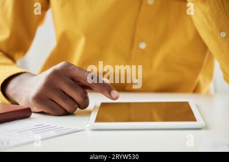 Focus on hand of black guy pointing at screen of tablet on desk while sitting in front of camera and making presentation of his project Stock Photo