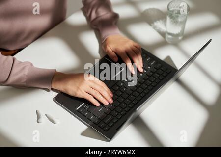 Above angle of hands of young female student or solopreneur pressing keys of wireless computer keyboard while sitting by her workplace Stock Photo