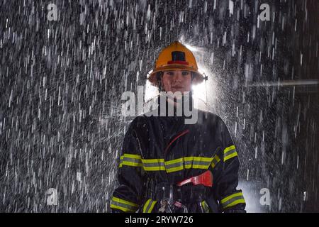 A determined female firefighter in a professional uniform striding through the dangerous, rainy night on a daring rescue mission Stock Photo