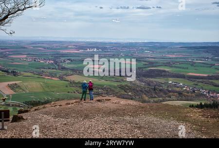 Donnersberg, Germany - April 9, 2021: Two women looking over the side of a mountain overlooking fields and small villages on a spring day at Adlerboge Stock Photo