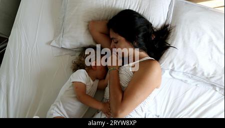 Mother cuddling and breastfeeding infant baby one year old toddler in bed Stock Photo