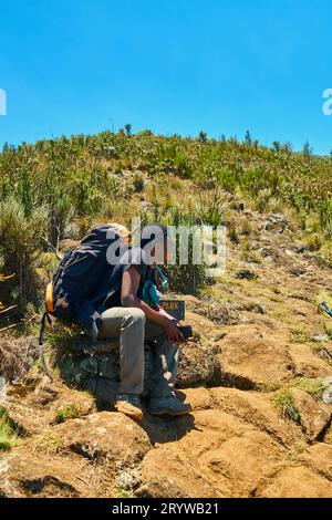 a dark-skinned guy with a backpack is resting in the mountains Stock Photo