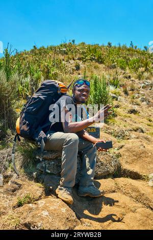 a dark-skinned guy with a backpack is resting in the mountains Stock Photo