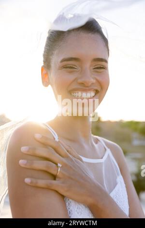 Closeup portrait of cheerful biracial young bride wearing veil at beach against clear sky Stock Photo