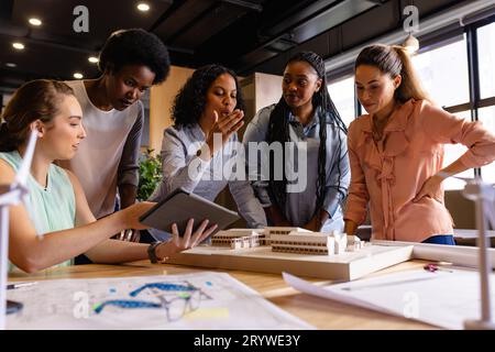 Diverse female architects in discussion using model, blueprints and tablet in casual office meeting Stock Photo