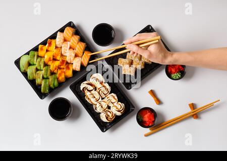 A set of bright sushi rolls with shrimp and salmon in plastic packages on a white background, a woman's hand takes the roll with Chinese chopsticks Stock Photo
