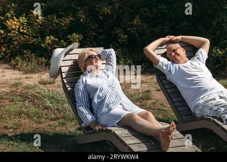 A couple of cute elderly people are lying on sunbeds, basking in the sun. Stock Photo