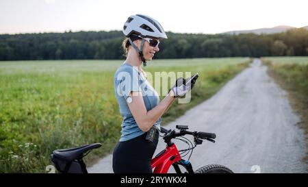 Diabetic cyclist with continuous glucose monitor checking on smartphone smartphone her blood sugar levels in real time. Stock Photo