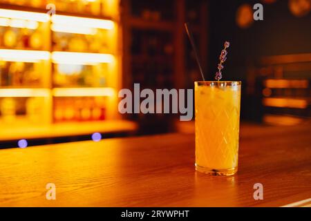 Crystal glass with orange cocktail and sprig of lavender on a bar blurred background. Free space for text Stock Photo