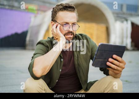 Shocked man reading information from tablet PC with frightened expression. Breaking news has caught him off guard. Facial expres Stock Photo