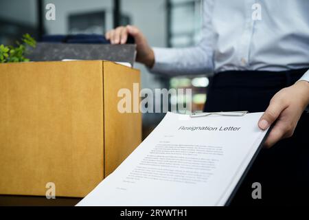 Business woman sending resignation letter to boss and Holding Stuff Resign Depress or carrying cardboard box by desk in office Stock Photo