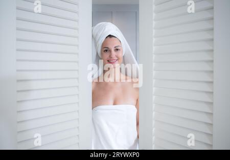 Portrait of a smiling young woman with towel on head opening the door of bathroom Stock Photo
