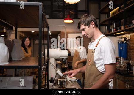 Portrait of a young male barista in apron using payment machine in cafe Stock Photo