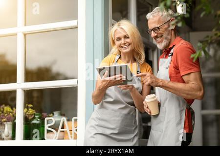 Modern Technologies. Smiling Mature Farmers Couple In Aprons Using Digital Tablet Together Stock Photo
