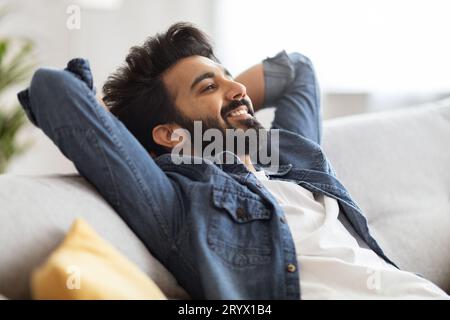 Relax Concept. Handsome Smiling Indian Man Leaning Back On Sofa At Home Stock Photo