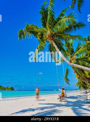 Praslin Seychelles tropical island with withe beaches and palm trees, couple men and woman in hammock swing on the beach under a Stock Photo