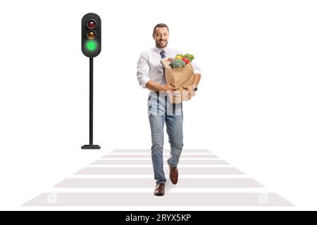 Full length portrait of a smiling professional man walking at a pedestrian and carrying a bag with fruits and vegetables isolated on white background Stock Photo