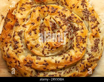 Freshly baked Burek made of filo dough with filling on baking paper background top view. Traditional savoury spiral pie of Balkans, Middle East and Stock Photo