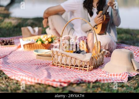 In love couple enjoying picnic time playing guitar in park outdoors Picnic. happy couple relaxing togetherÂ with picnic Basket Stock Photo