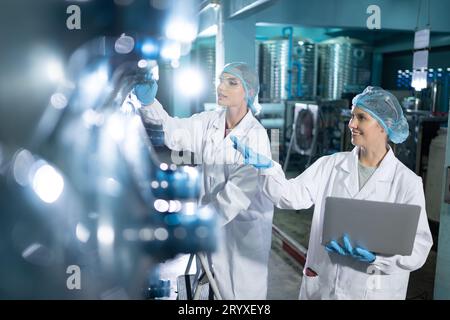 Portrait of a scientist in the drinking water factory using a ladder, looking at the water tanks above and examining with a coll Stock Photo