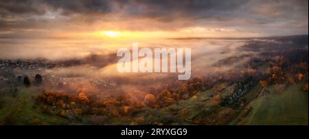 Highly dramatic sunrise scenery from above the fog. Panoramic aerial view of a beautiful landscape with magnificent red light illuminating dark clouds Stock Photo