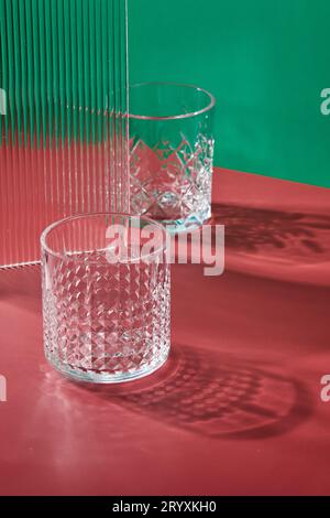 Two empty glass glasses on colored backgrounds with shadows from sunlight Stock Photo