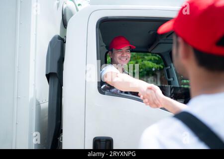 Delivery man in red cap and uniform handshaking each other after finishing deliveries. Stock Photo