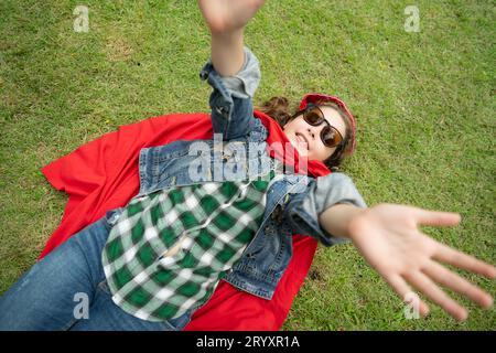 On a beautiful day in the park, a young girl enjoys her vacation. Playful with a red superhero costume and mask. Stock Photo
