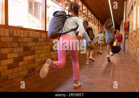 Diverse schoolgirls with bags running in elementary school corridor Stock Photo