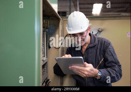 Senior engineer inspects the electrical system and repairs the mechanical system in the machine control cabinet. in order for th Stock Photo