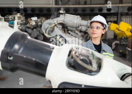 A female engineer installs a program on a robotics arm in a robot warehouse. And test the operation before sending the machine t Stock Photo
