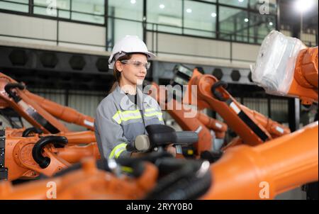 After installing a program on the robotic arm, a female engineer with a robotic arm controller performs a test run. Stock Photo