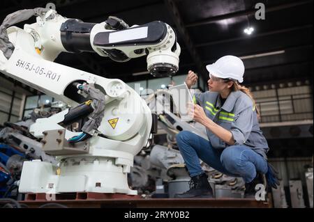 A female engineer installs a program on a robotics arm in a robot warehouse. And test the operation before sending the machine t Stock Photo