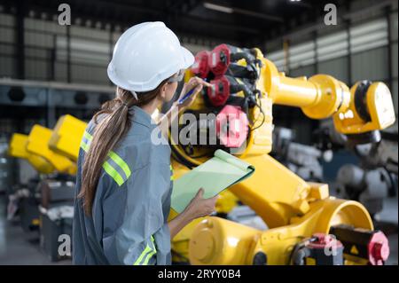 A female engineer checking documented items after installing a program on a robotic arm in a robotic warehouse and test the oper Stock Photo