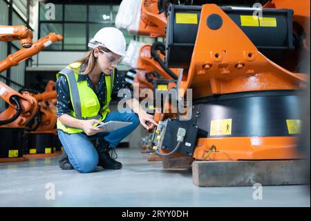 Female Technician Inspecting and repairing robotics arm in robots hangar and test the operation of the machine after being used Stock Photo