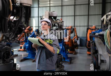A female engineer checking documented items after installing a program on a robotic arm in a robotic warehouse and test the oper Stock Photo